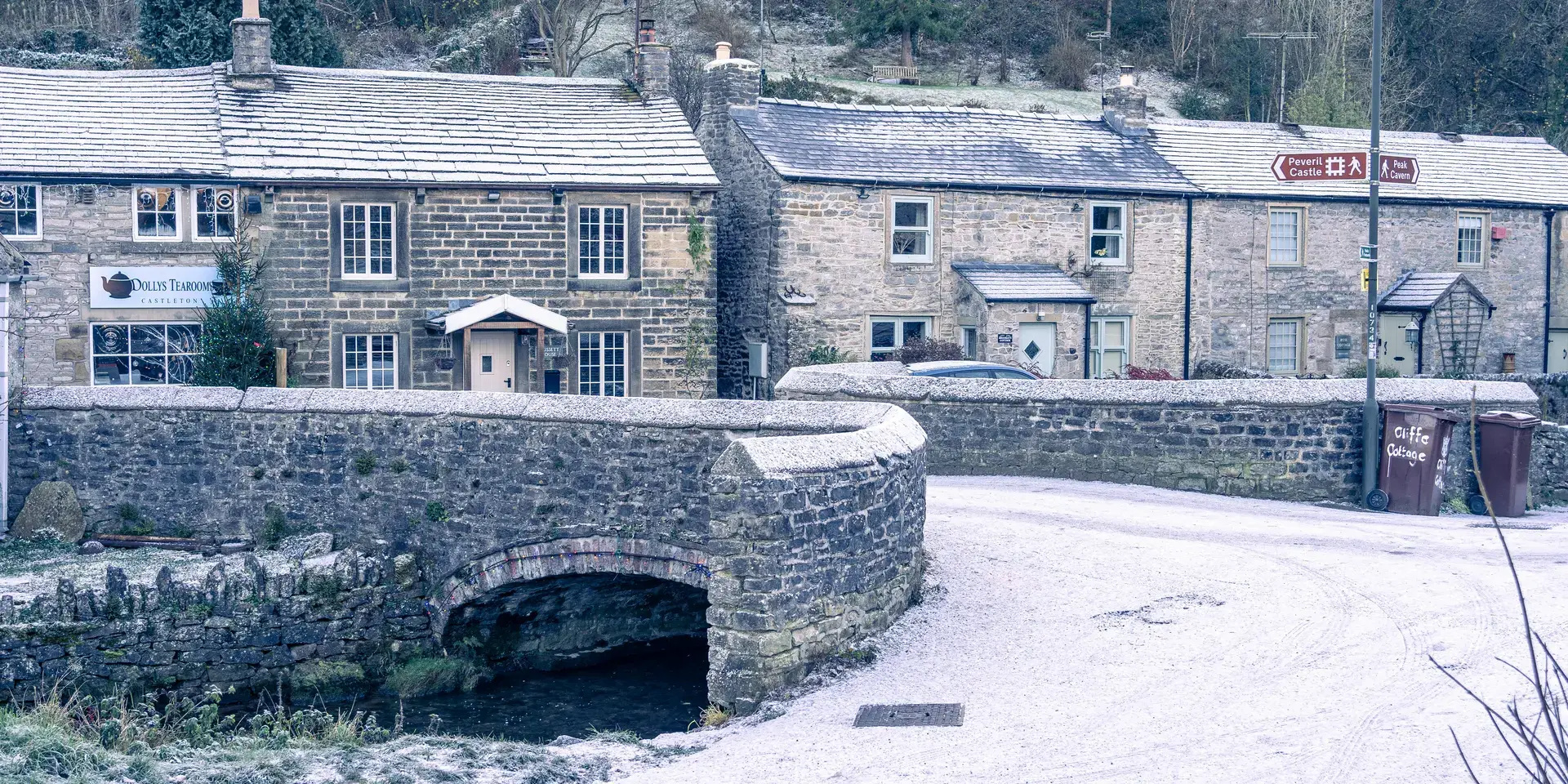 Snow-dusted stone cottages and a bridge over a small stream in a quaint winter village setting