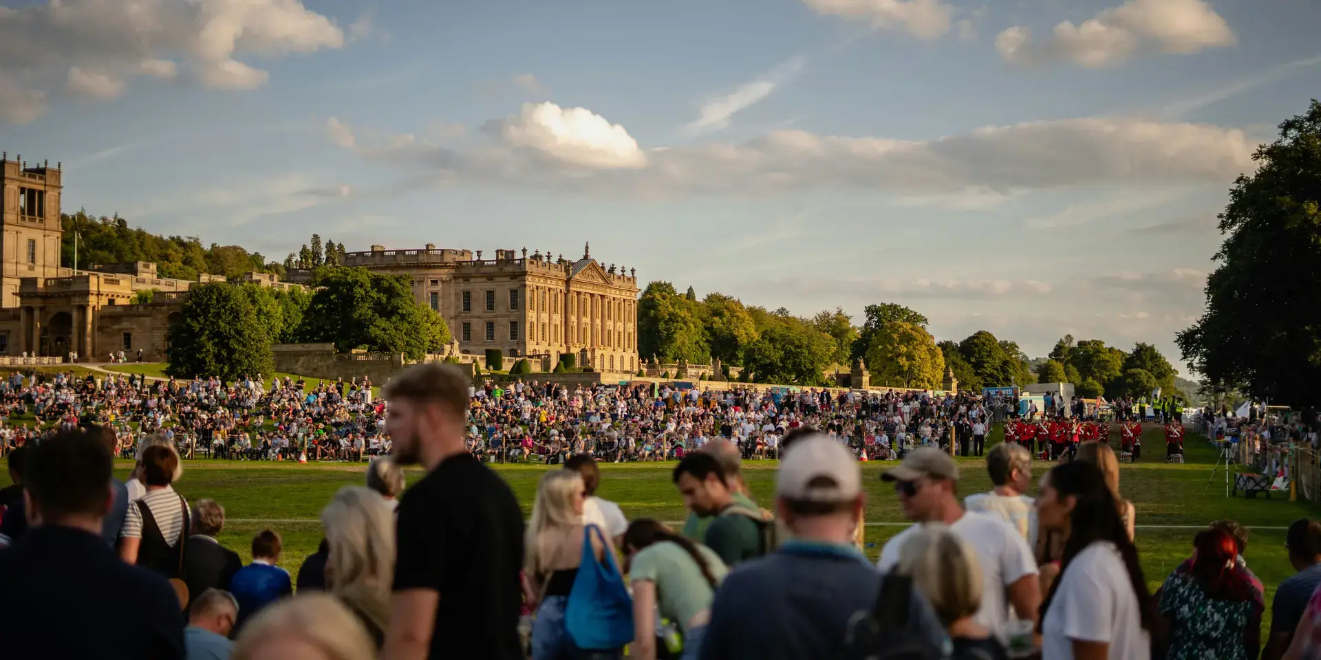 Large crowd gathered on a sunny day in front of a grand historic building, enjoying an outdoor event under a blue sky