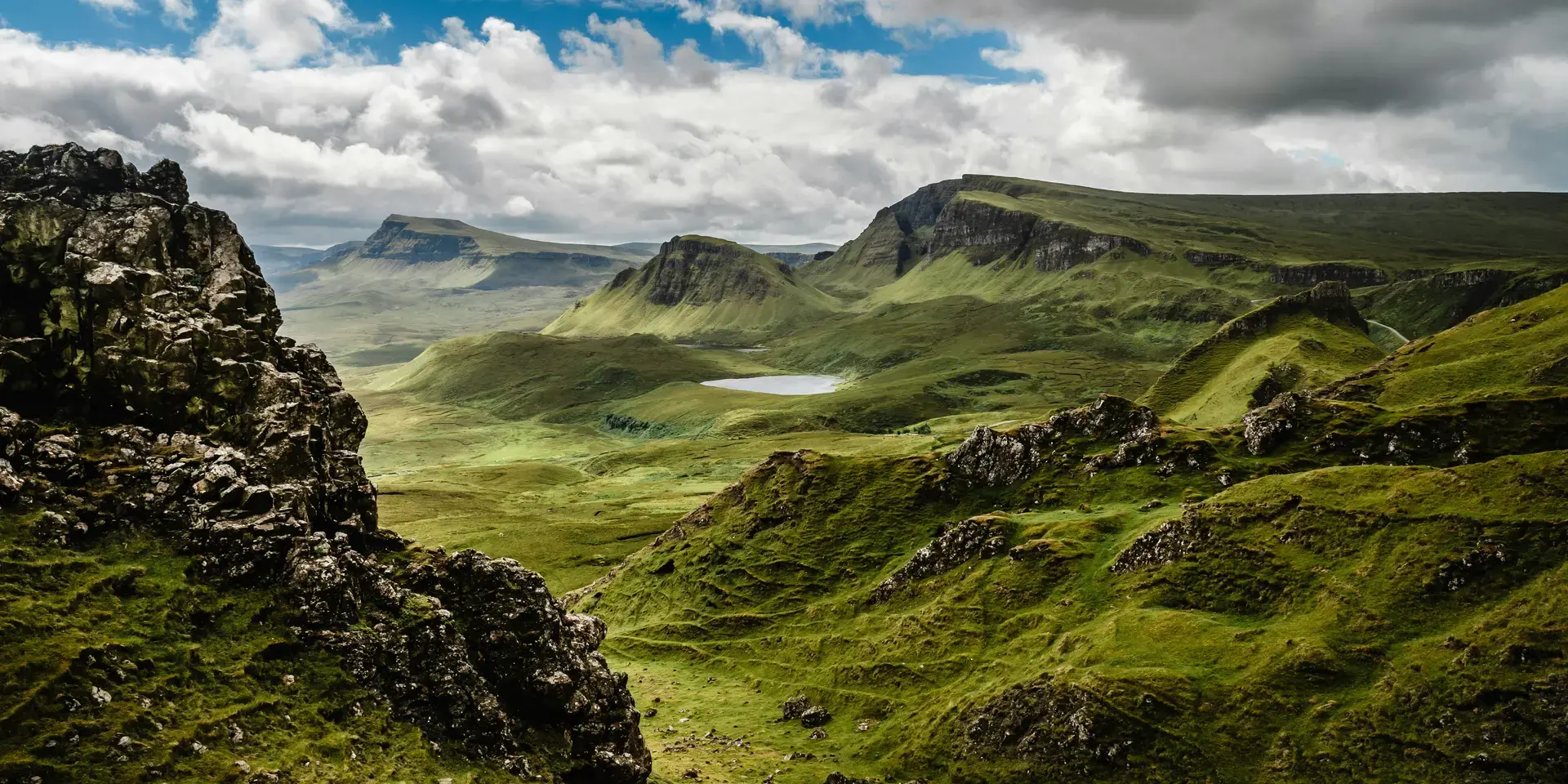 Rolling green hills and dramatic cliffs of Scotland’s Quiraing under a cloudy sky, a serene and rugged Highland landscape