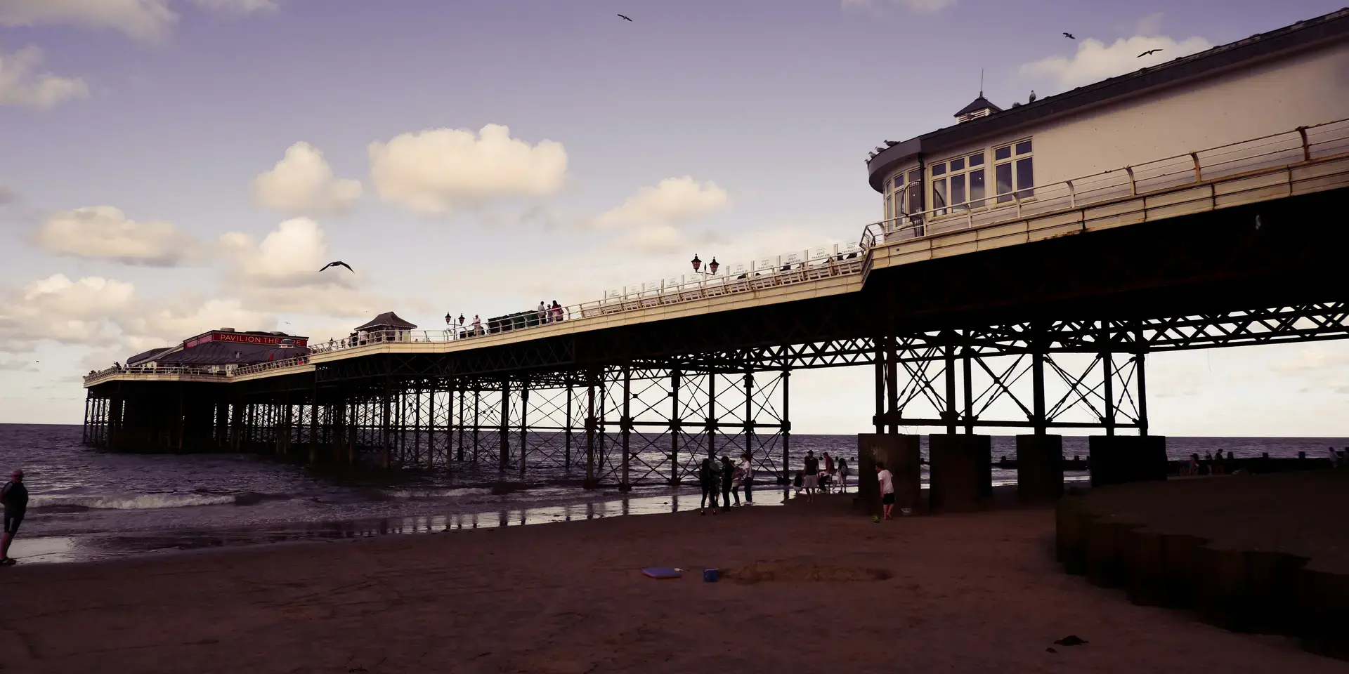 Victorian pier stretching over the sea,with Pavilion Theatre and visitors enjoying a seaside stroll under a purple-tinged sky