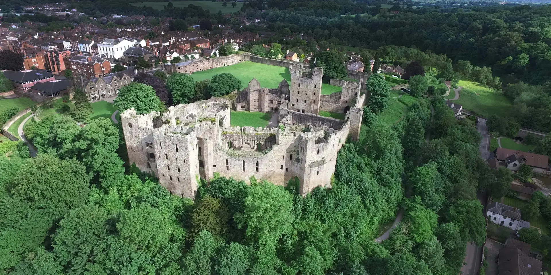 Majestic stone castle surrounded by lush green forests, overlooking a quaint village under a bright, clear sky