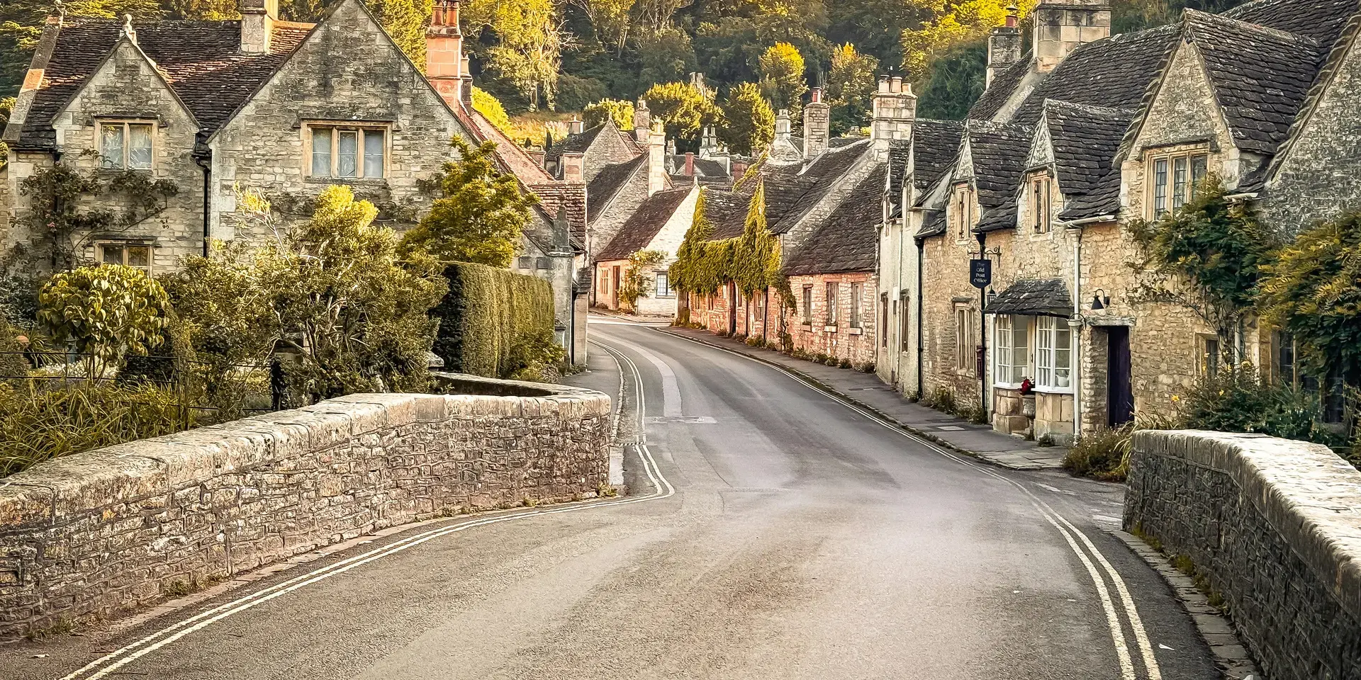 Charming English village road with stone houses, ivy-clad walls, and lush greenery, illuminated by golden evening sunlight