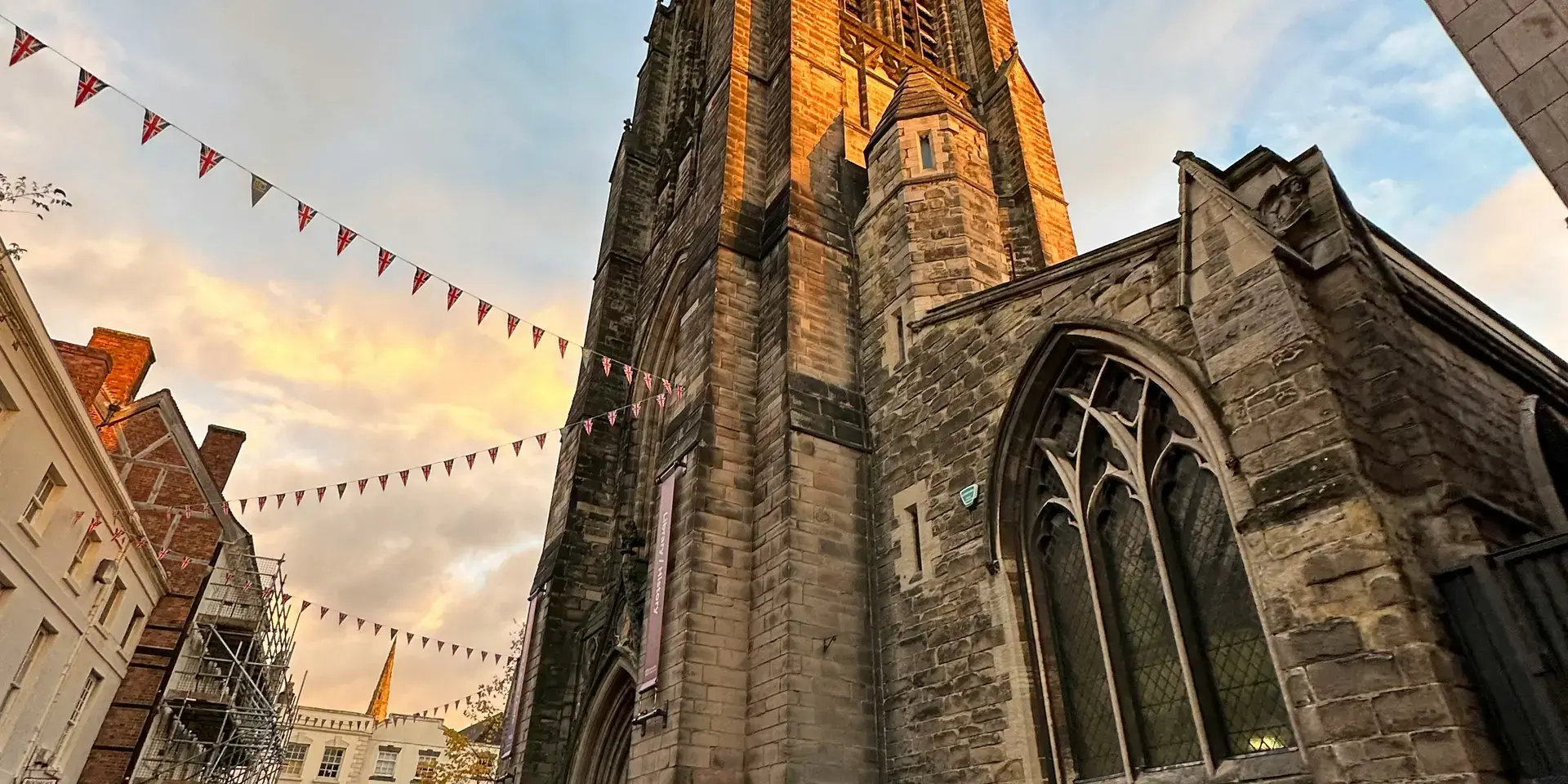 Gothic church tower glowing in sunset light, cobbled street below, festive bunting adds charm to the scene