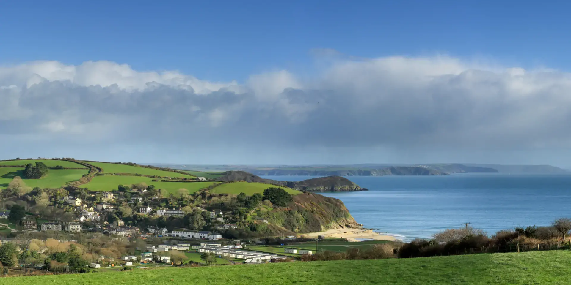 Scenic coastal landscape with a small village nestled among green hills overlooking a calm blue sea under a partly cloudy sky