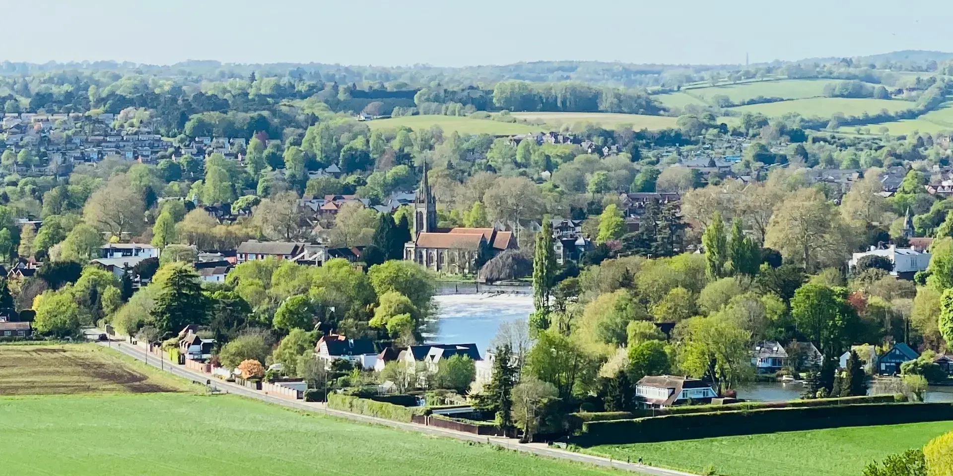 Serene village with a church, green fields, trees, and hills in the distance under a bright, clear sky