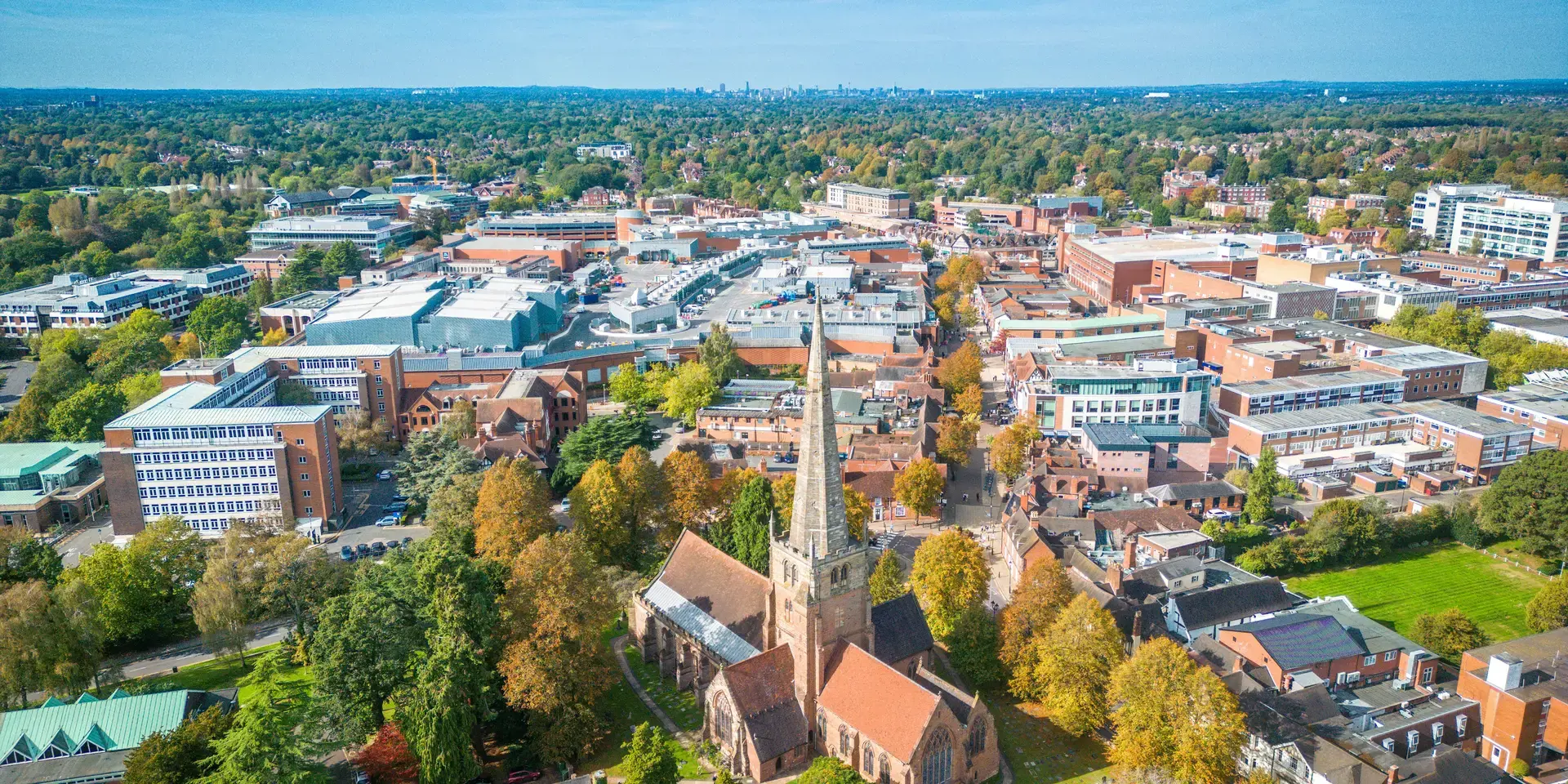 An aerial view of a bustling town with a historic church in the foreground, surrounded by greenery and modern buildings