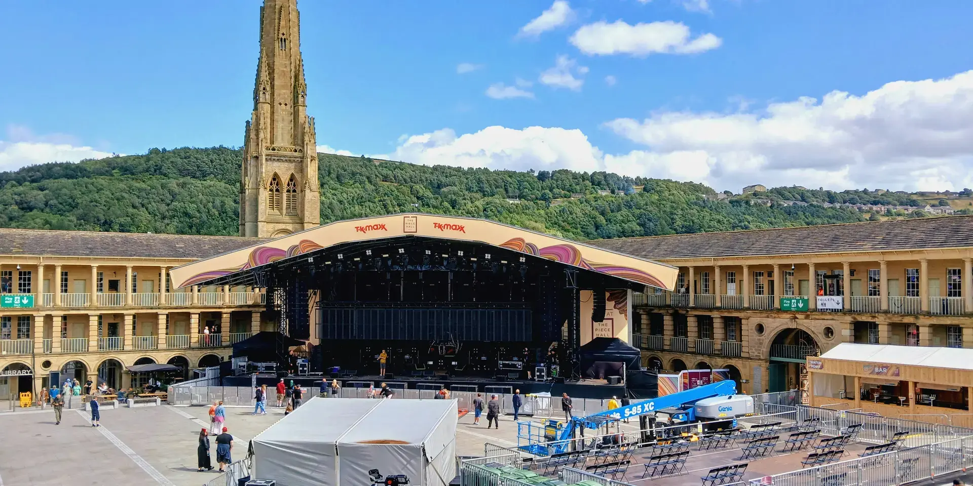 The Piece Hall in Halifax hosts an event, featuring a grand stage, surrounded by hills and a vibrant blue sky