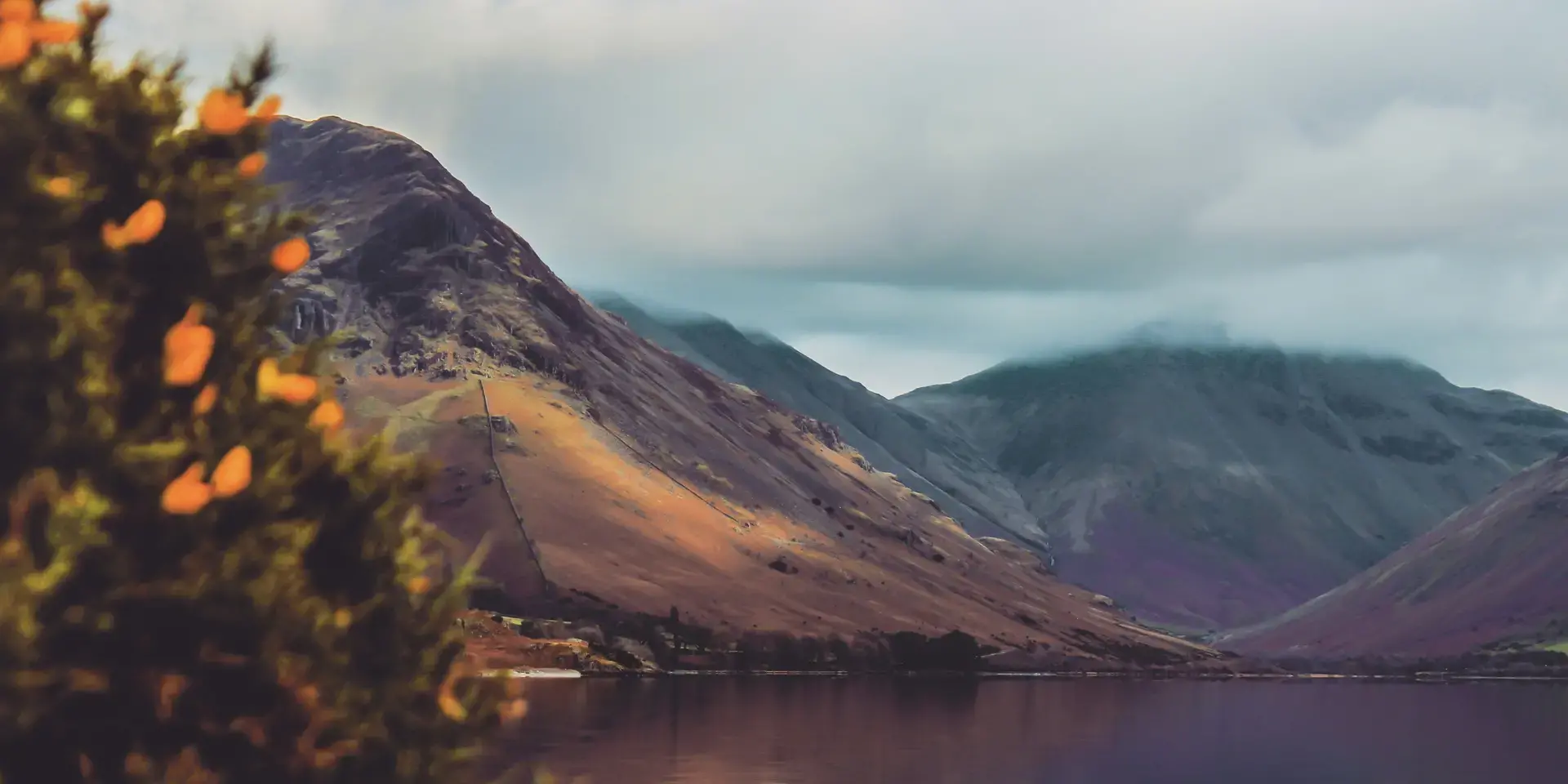 Mountain landscape reflected in a calm lake, with soft clouds and warm tones.