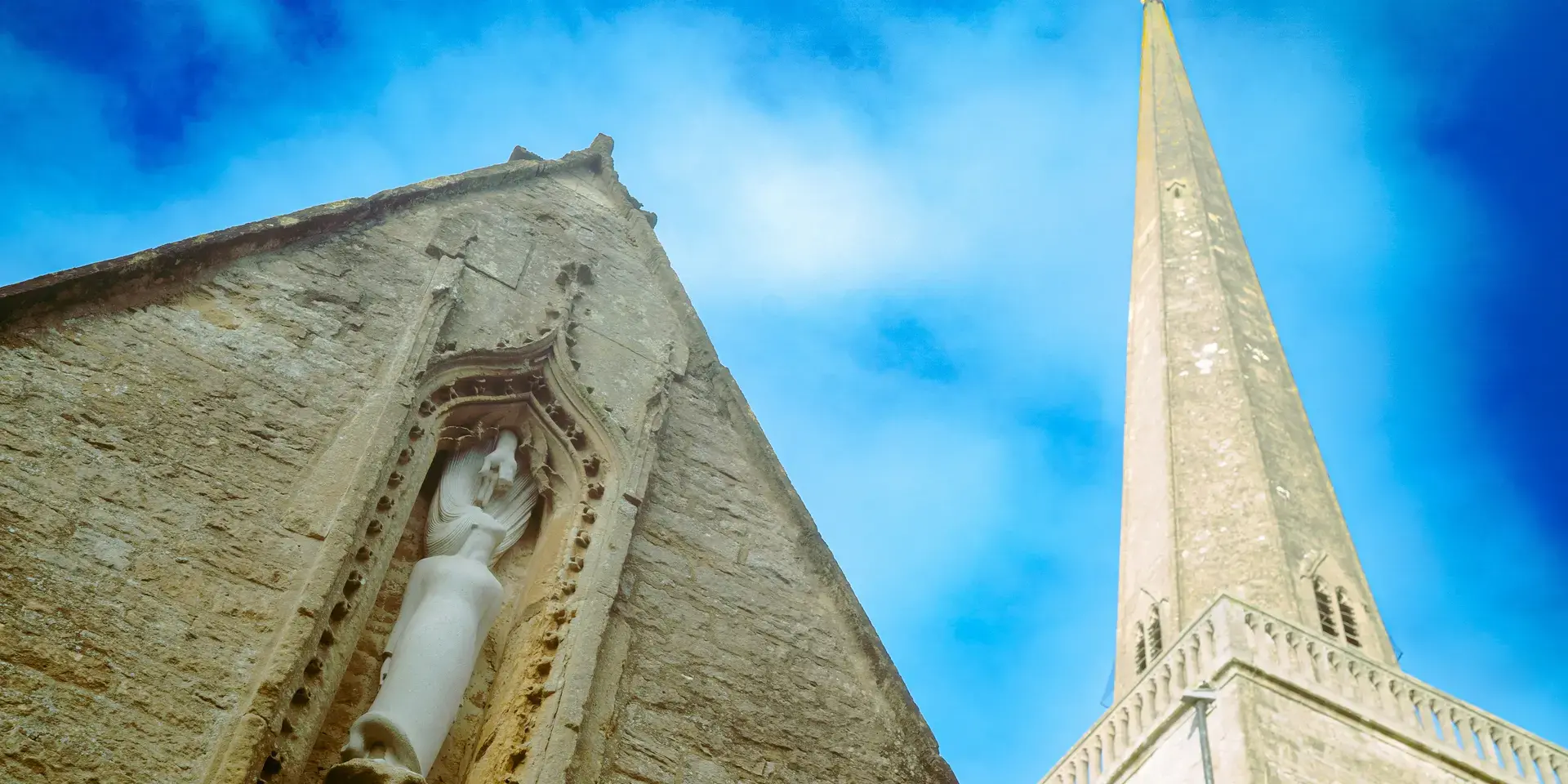 Close-up of a stone church with intricate sculpture detail, alongside its tall spire reaching into a bright blue sky