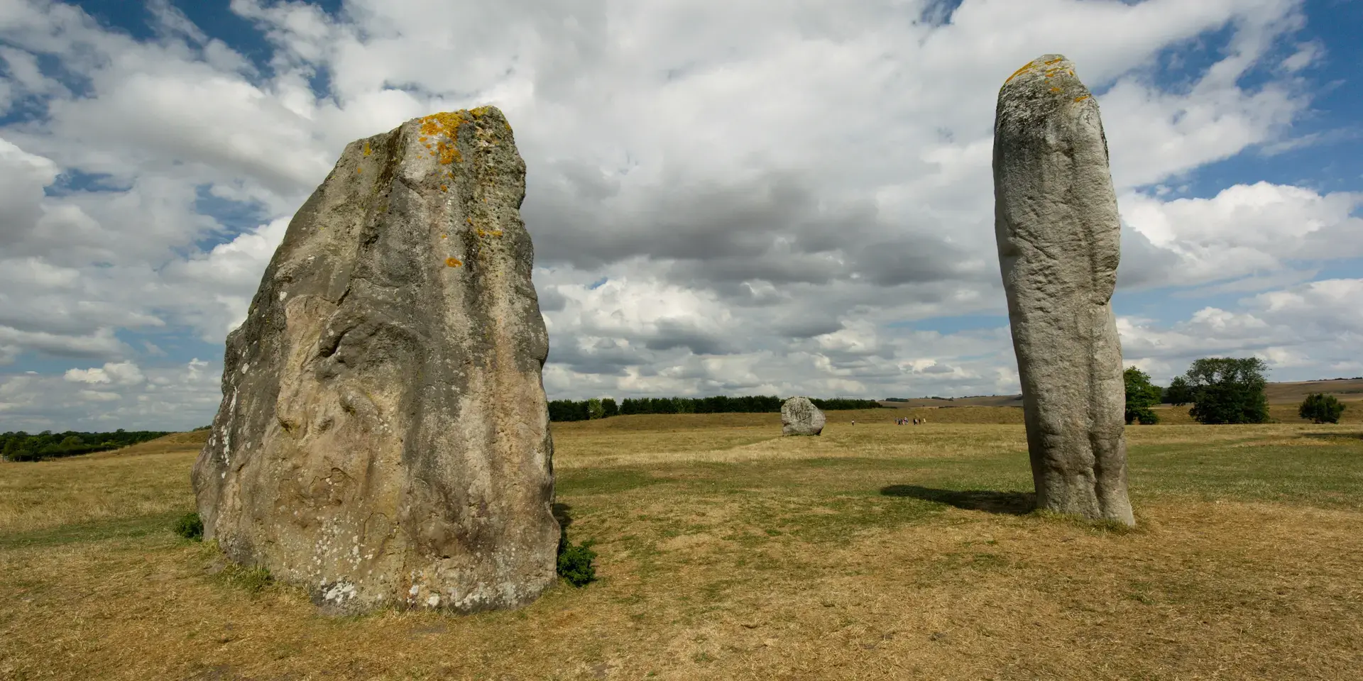 Ancient standing stones at Avebury henge, Wiltshire, surrounded by open fields, under a vast, cloud-filled sky