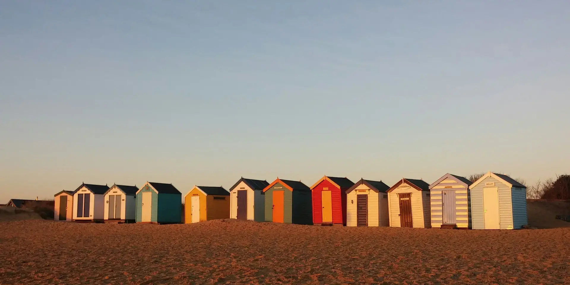 Colorful beach huts on golden sands, basking in the warm glow of a sunset under a clear evening sky
