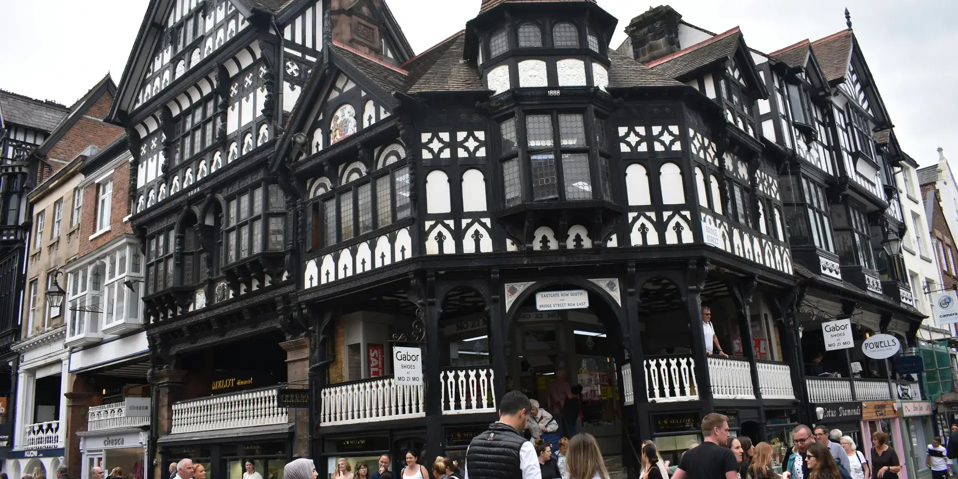 Crowd walking by a historic black-and-white timbered building, featuring intricate architecture and a vibrant atmosphere.