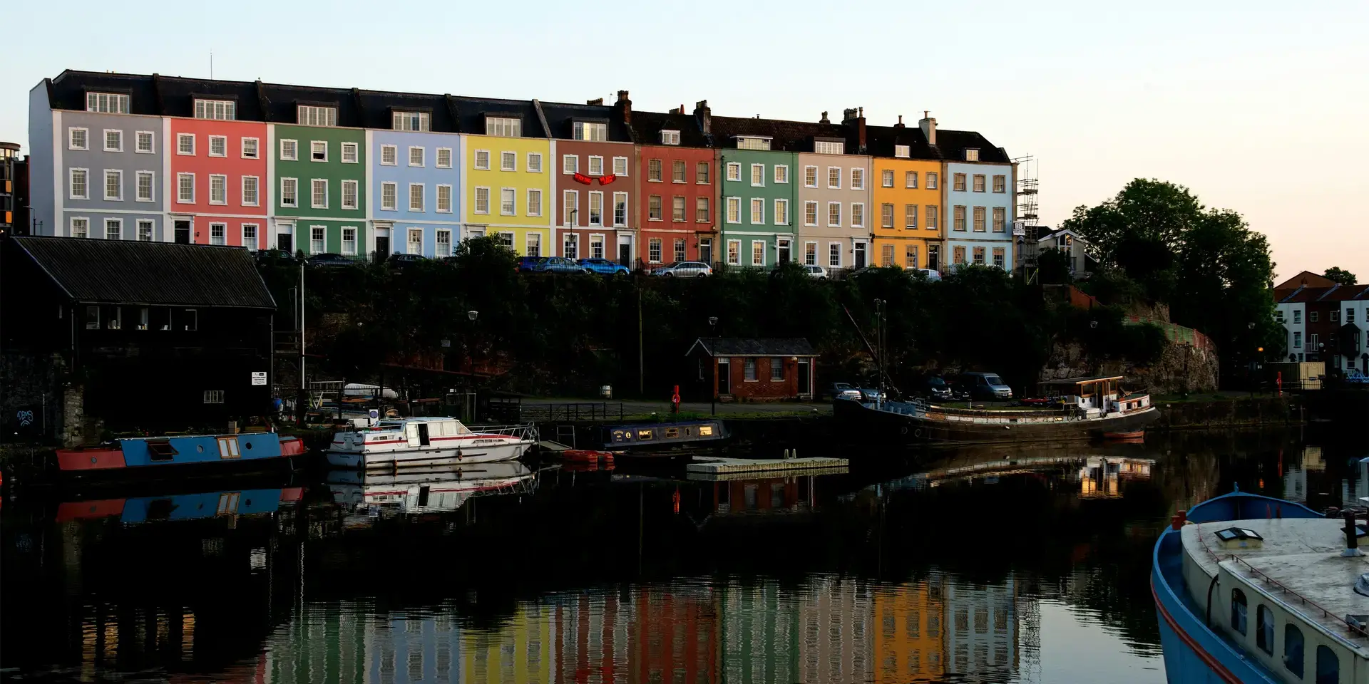 Colorful houses in Bristol reflect on the calm waters of the harbor, creating a vibrant and picturesque evening scene