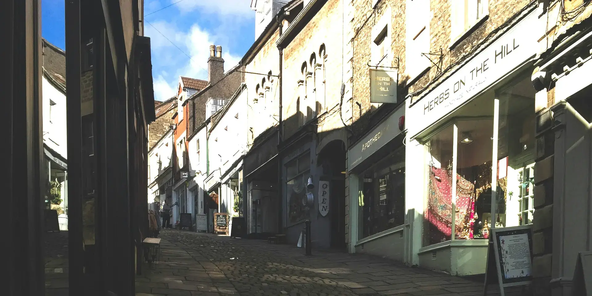 Charming cobblestone street lined with small shops and a sign reading ‘When in Frome’ promoting independent shopping