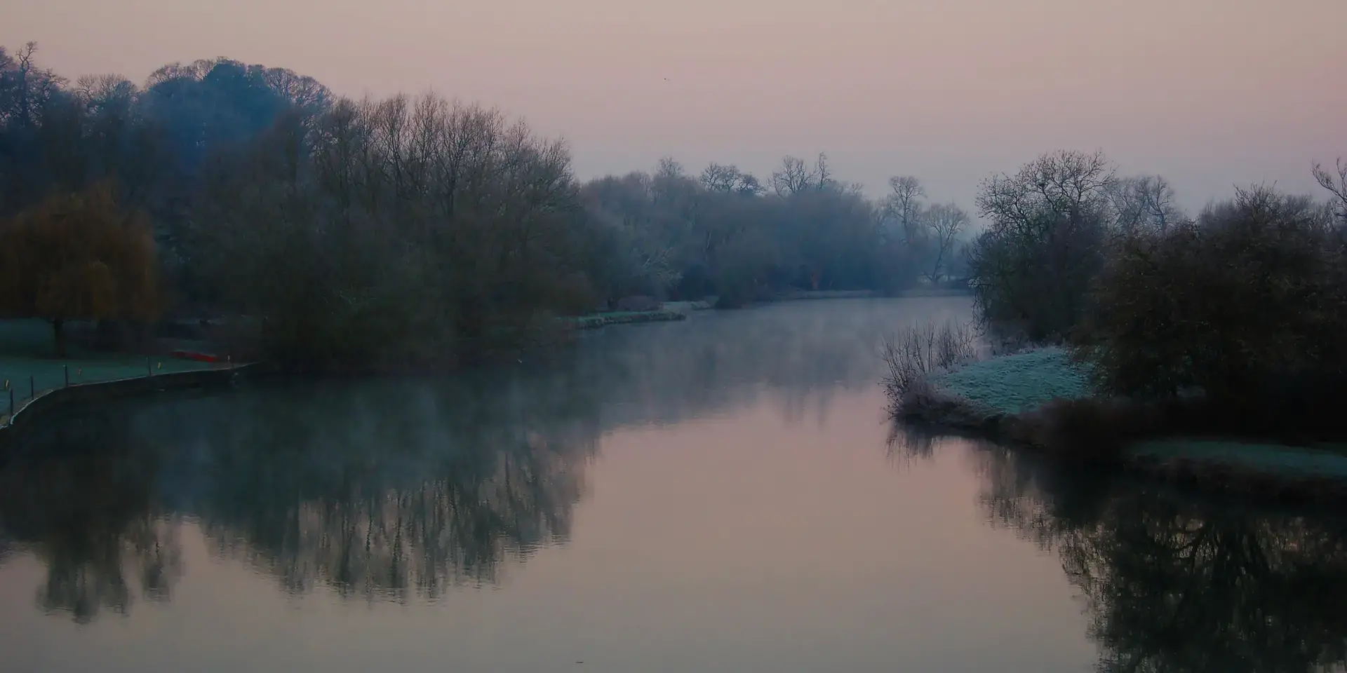 Peaceful river surrounded by frosty trees under a pastel pink and blue sky during dawn
