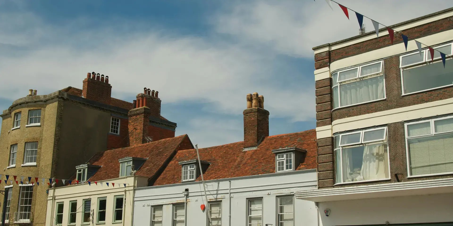 Charming townhouses with red brick chimneys under a bright blue sky, adorned with festive bunting in red, white, and blue