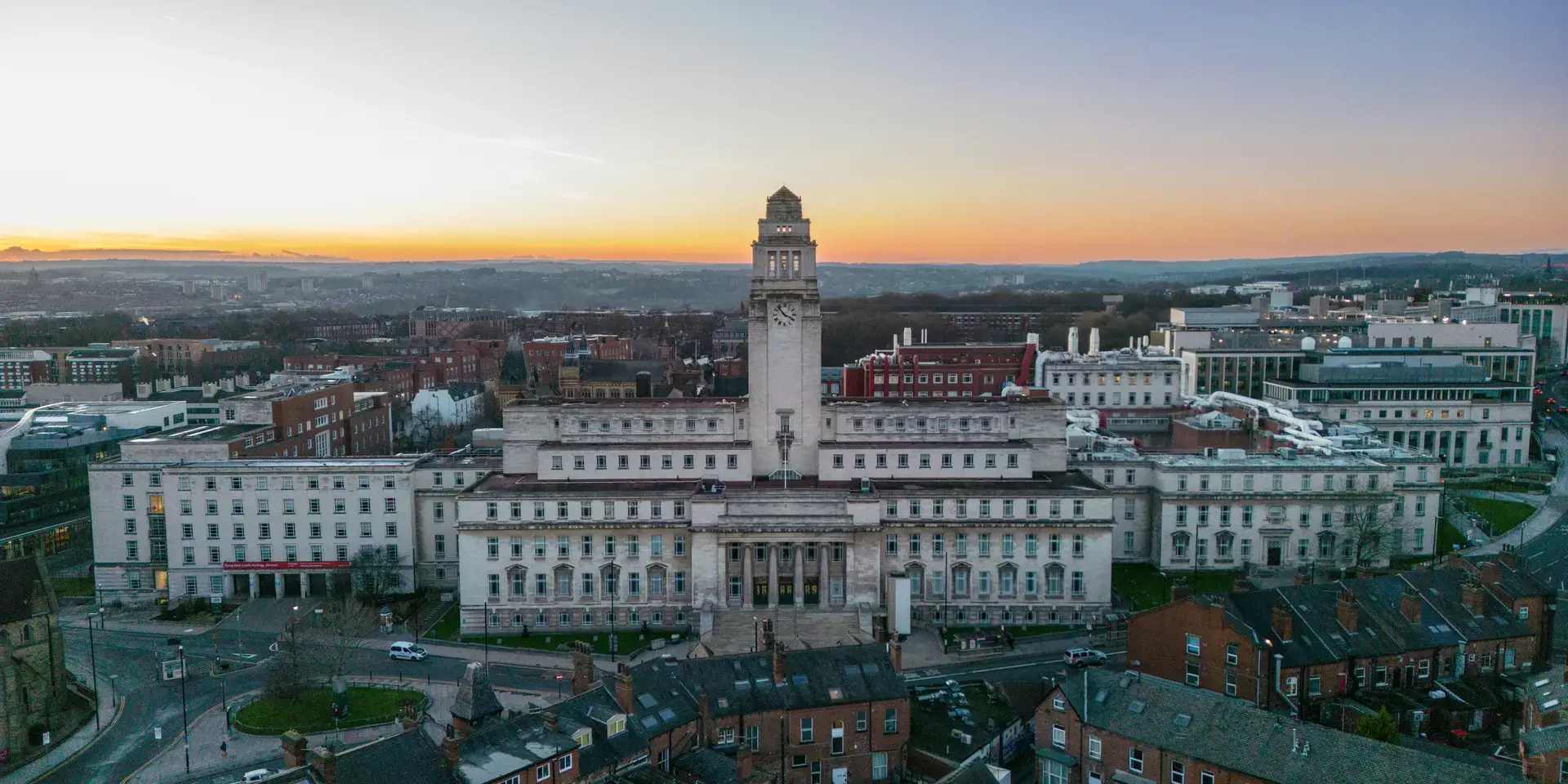 Sunset view of a historic university building, surrounded by city rooftops and modern architecture stretching to the horizon