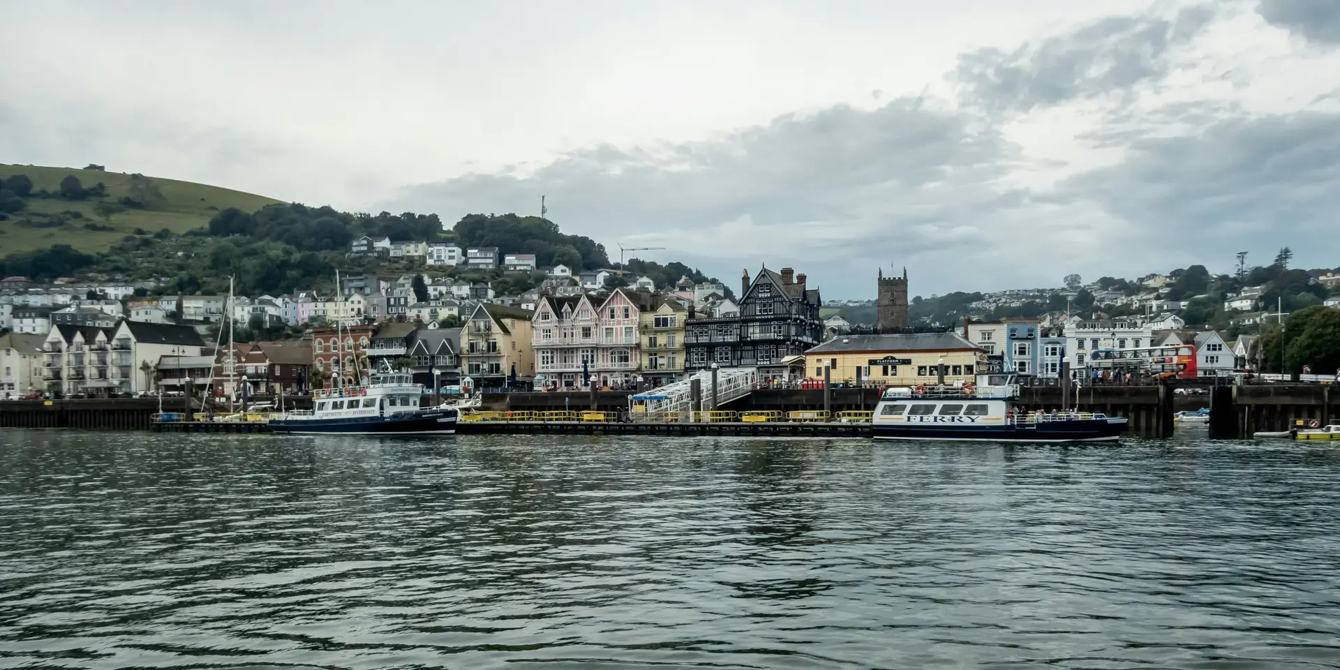 Charming waterfront town with pastel buildings, a historic black-and-white structure, and ferries docked by the scenic bay