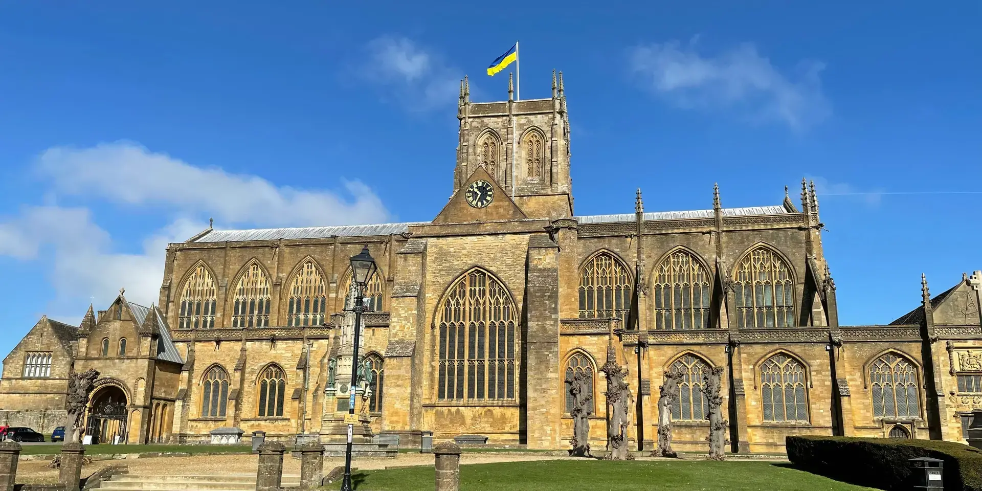 Historic stone church with tall arched windows and a clock tower flying the Ukrainian flag under a clear blue sky