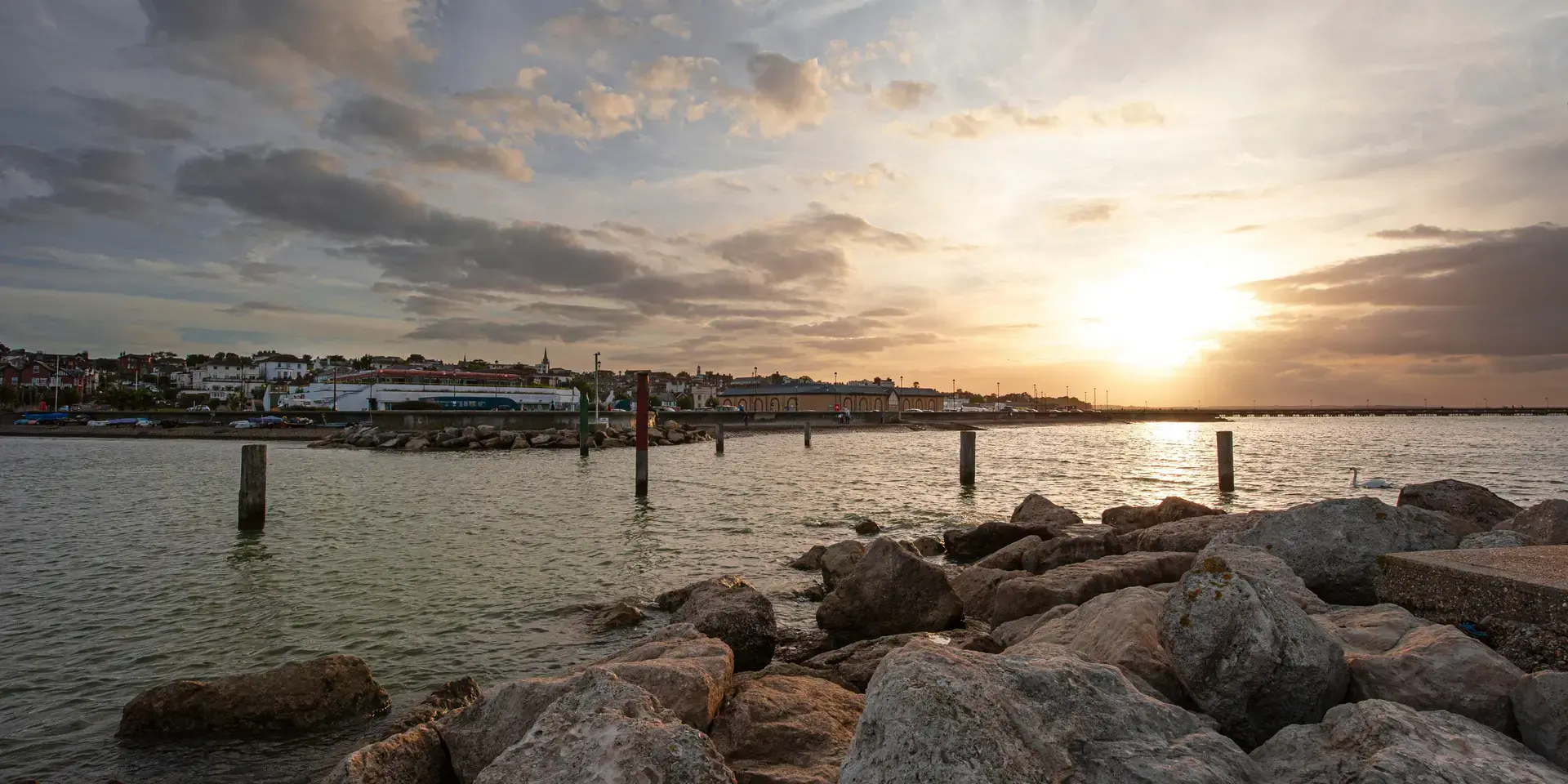Sunset over a calm coast, waves hit the rocks gently. A serene moment by the sea as the town glows under the fading light