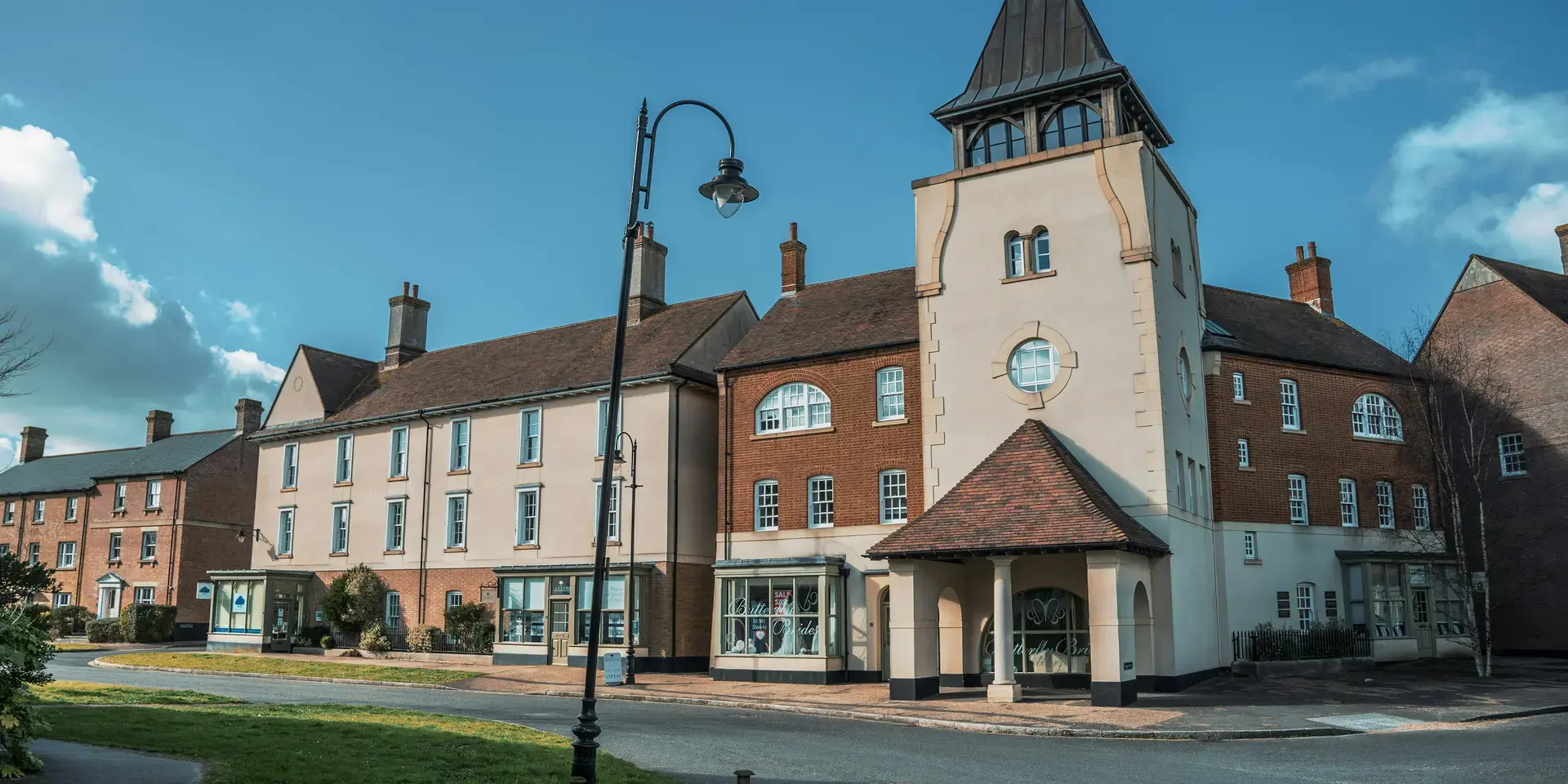 Charming village scene with a classic clock tower, quaint buildings, and lush greenery, all under a bright blue sky