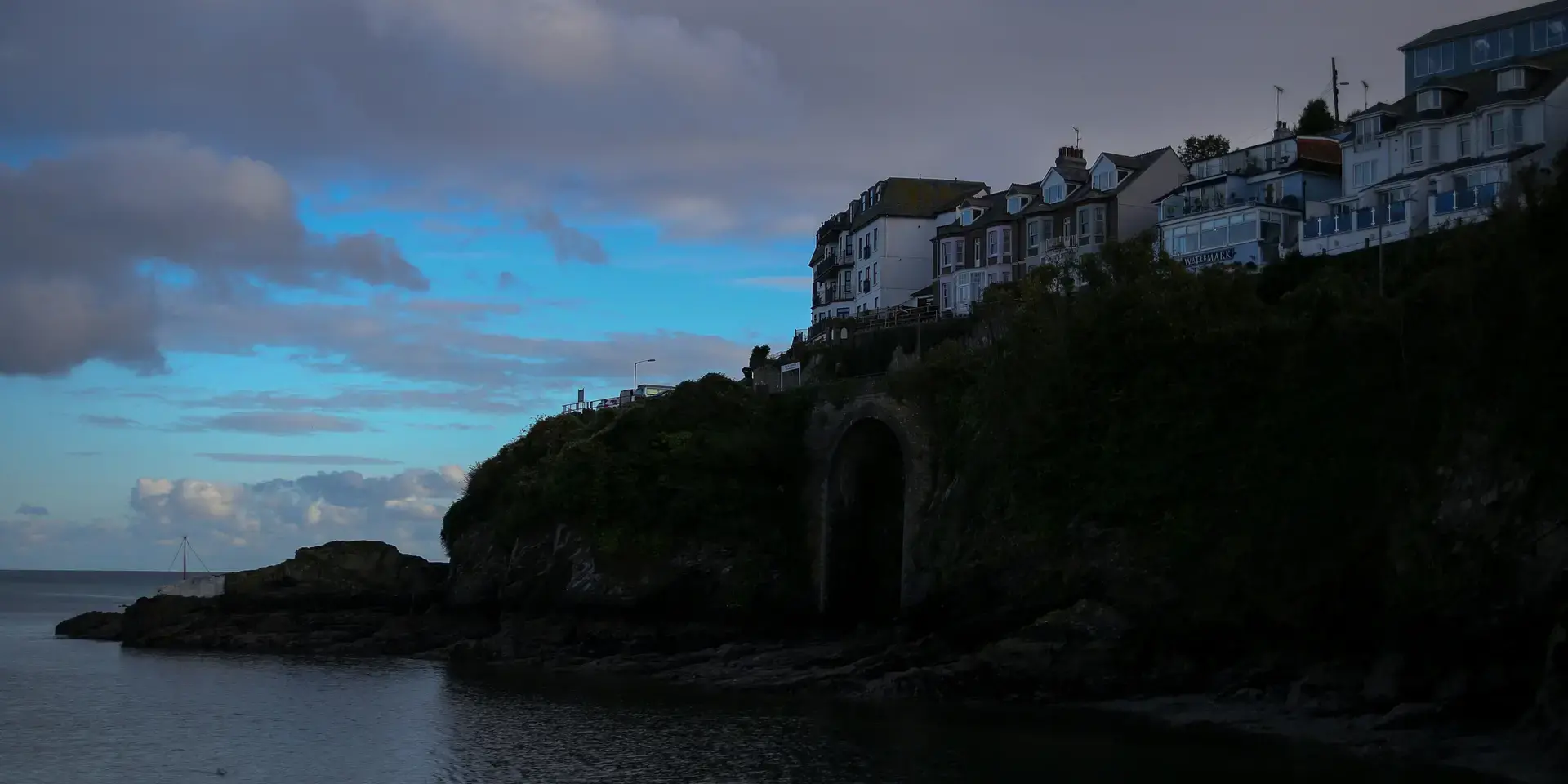 Silhouette of coastal houses on a cliff at dusk with a calm sea and cloudy sky