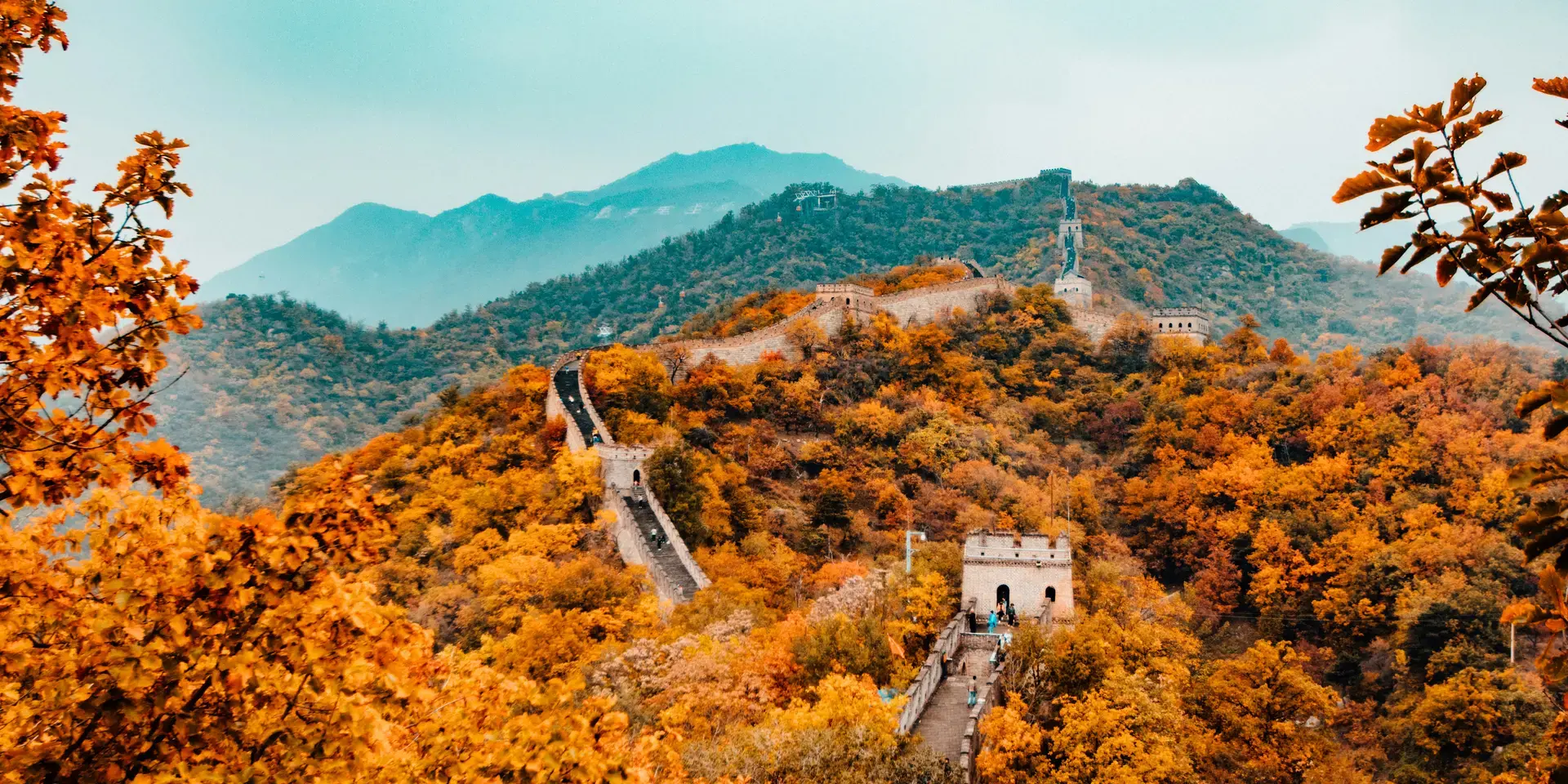 Great Wall of China winding through vibrant autumn foliage under a misty sky, showcasing its historical grandeur