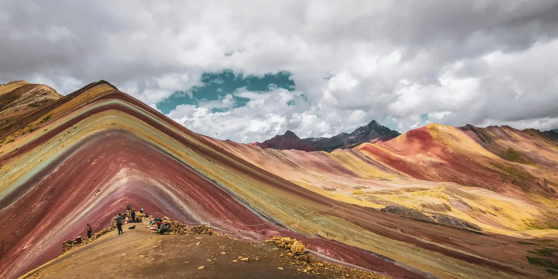 Vivid Rainbow Mountain in Peru, showcasing stunning layers of red, yellow, and green hues under a dramatic cloudy sky