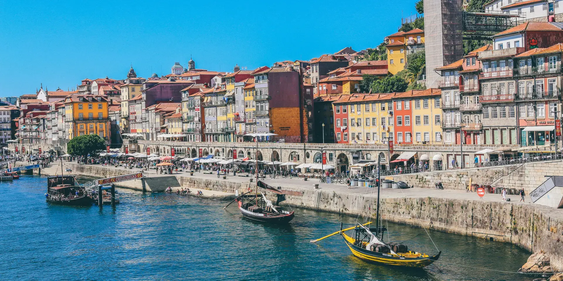 Colorful riverside houses and traditional boats in Porto, Portugal, along the scenic Douro River under a bright blue sky
