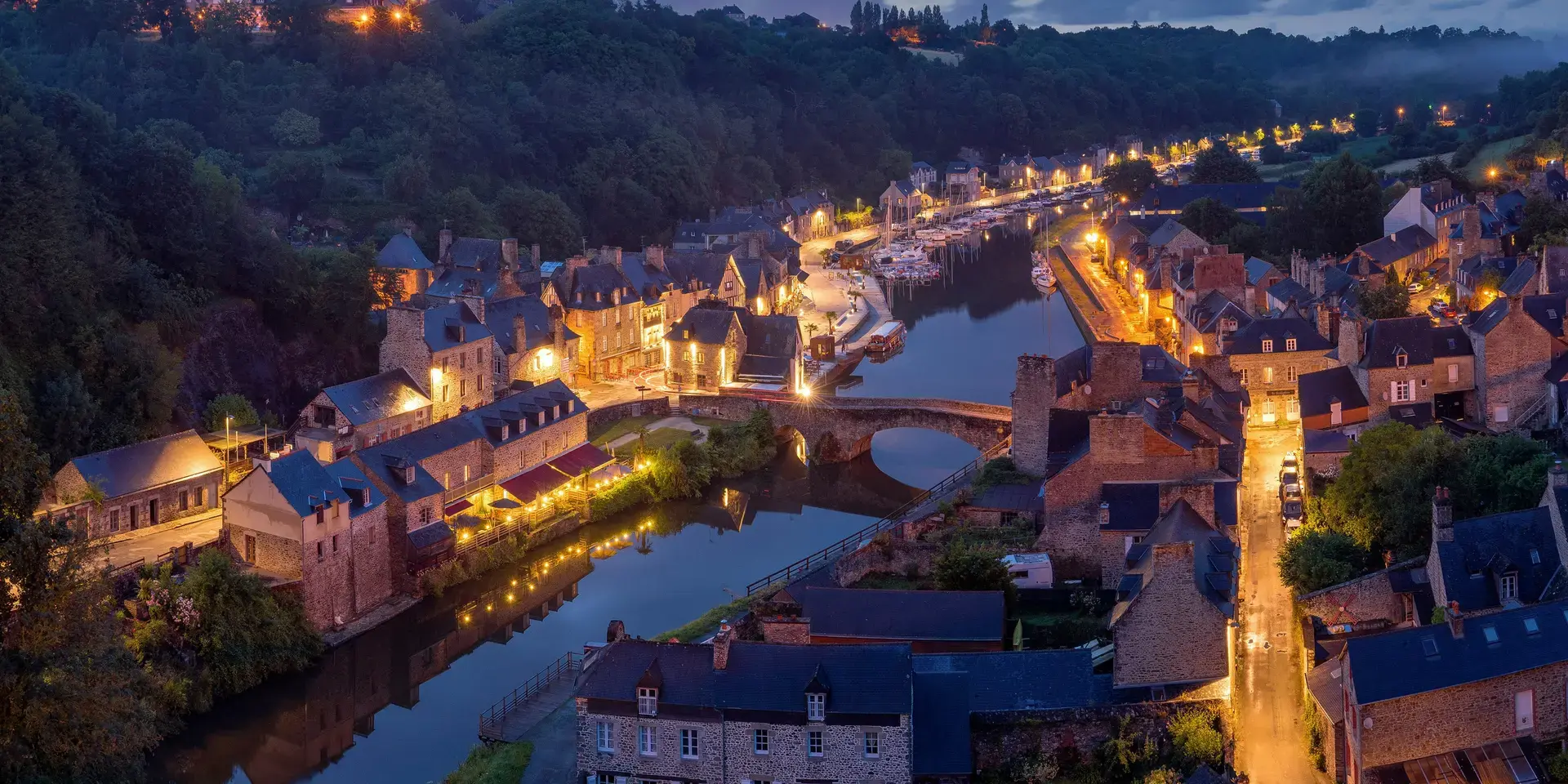 Charming medieval village at night, with illuminated streets, stone houses, and a peaceful river reflecting the warm lights