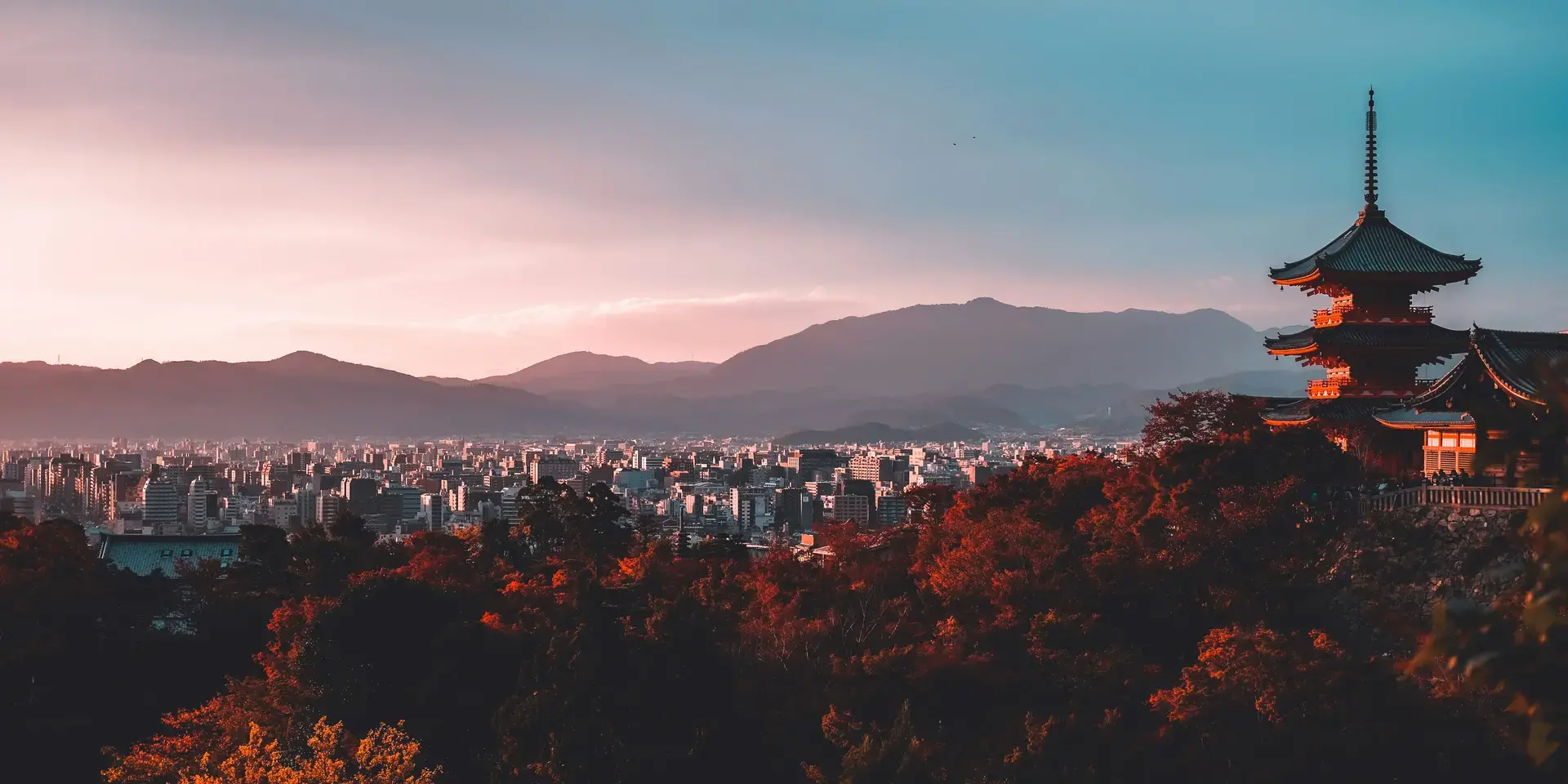 Kyoto cityscape at sunset with a traditional pagoda in the foreground and mountains in the distance