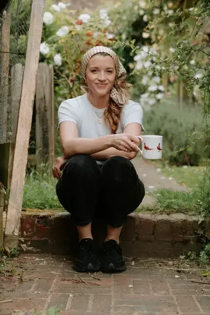 Lucy Sally Sommer sitting on a garden step, holding a mug.