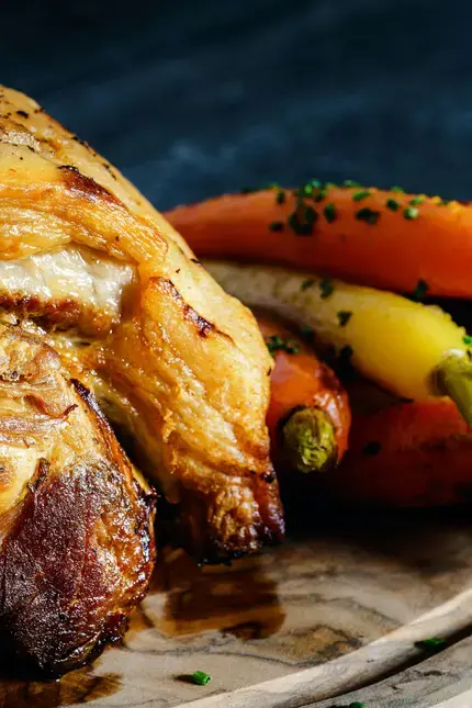 Roasted meat with golden and orange carrots served on a rustic plate.