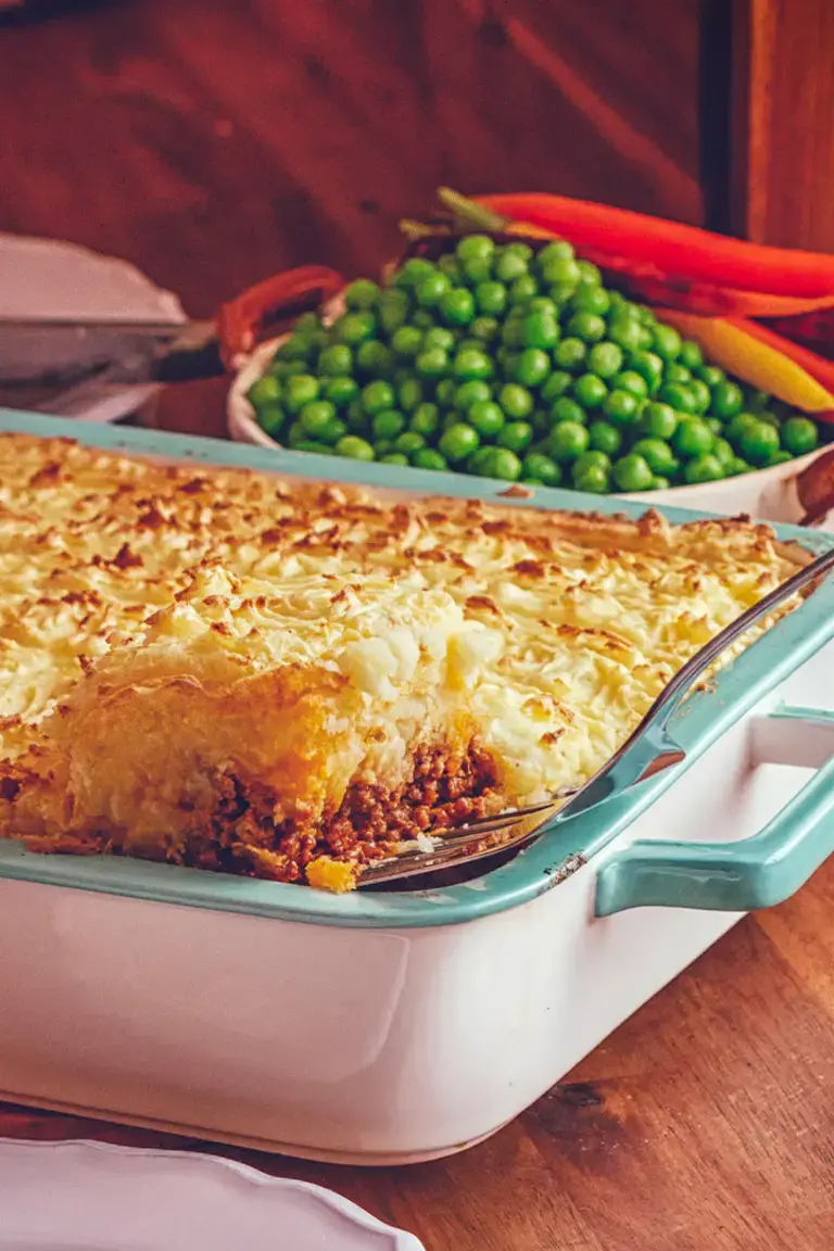 Someone spooning cottage pie from a casserole dish.