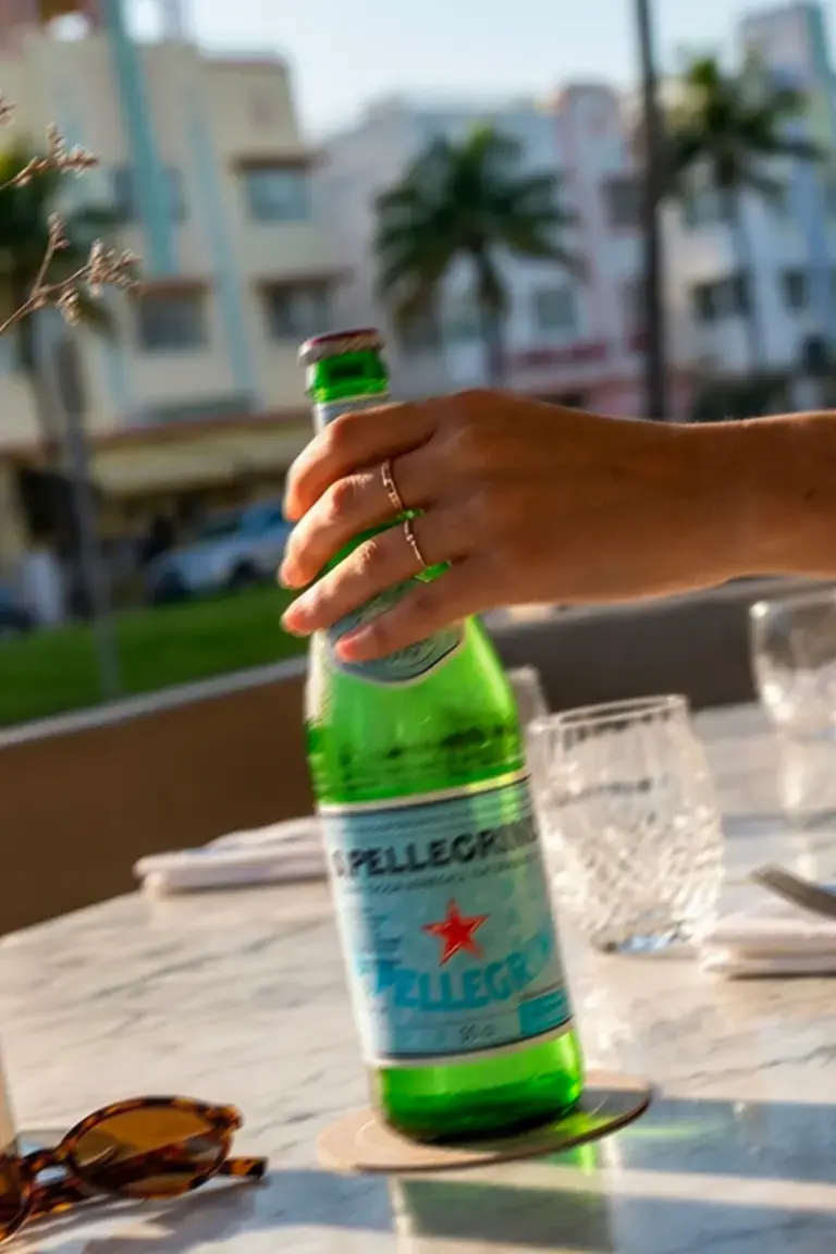 A hand holding a S.Pellegrino bottle on a Miami restaurant terrace.
