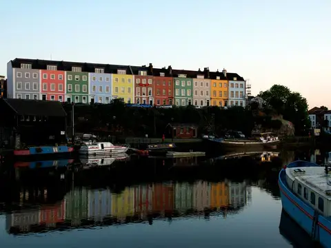 Colorful houses in Bristol reflect on the calm waters of the harbor, creating a vibrant and picturesque evening scene
