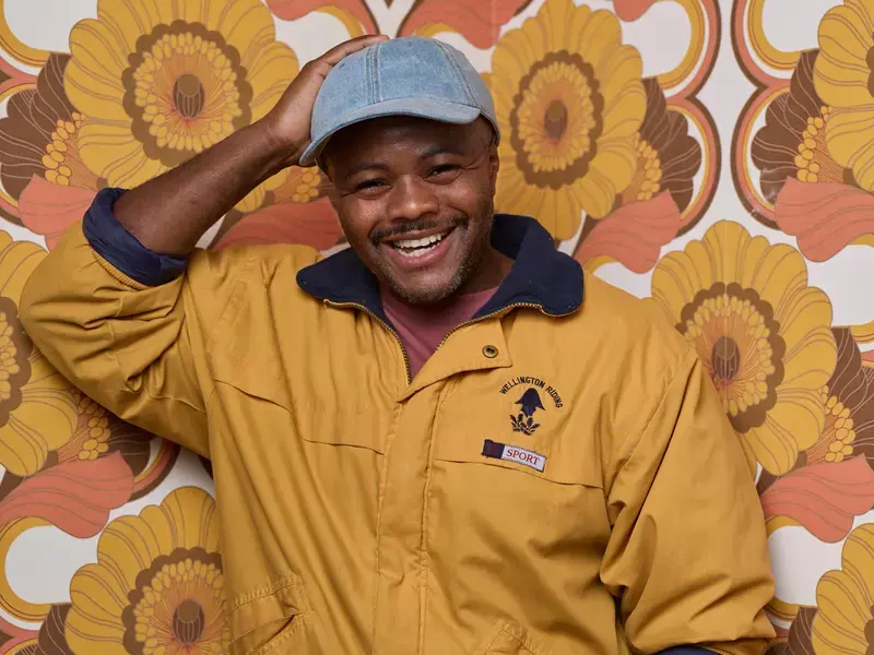 Chef Dom Taylor smiling against colourful wallpaper.