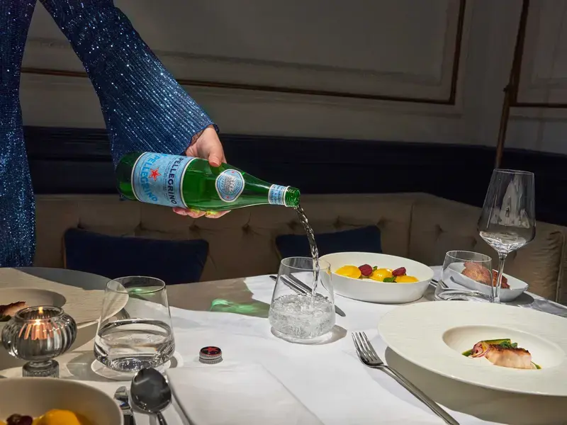 A girl pours S.Pellegrino water into a bottle.