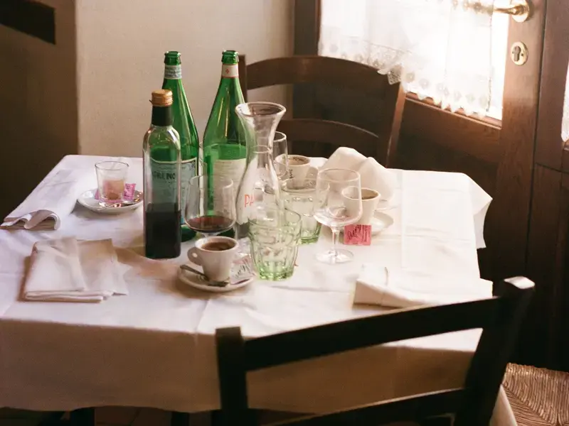 A restaurant table with empty water bottles, wine glasses and coffee cups.
