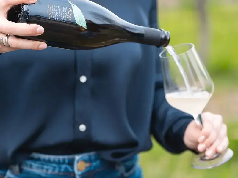 A person pouring a Feral drink into a wine glass.