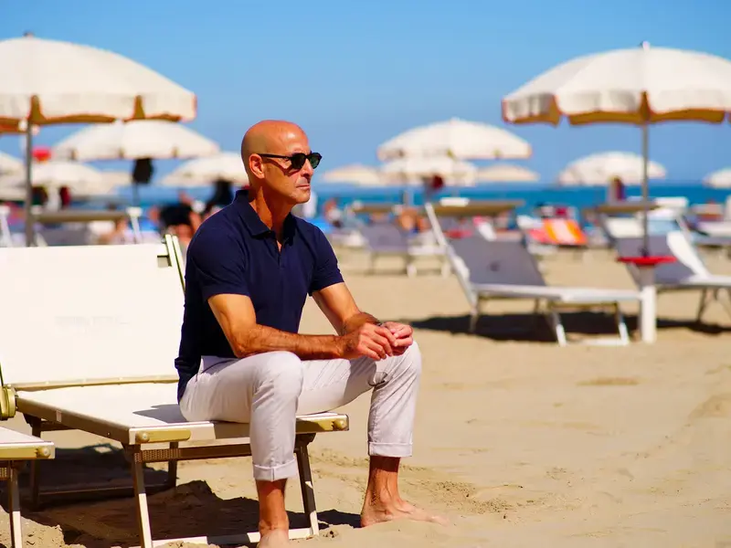 Stanley Tucci sat on a sun lounger on a sandy, sunny beach
