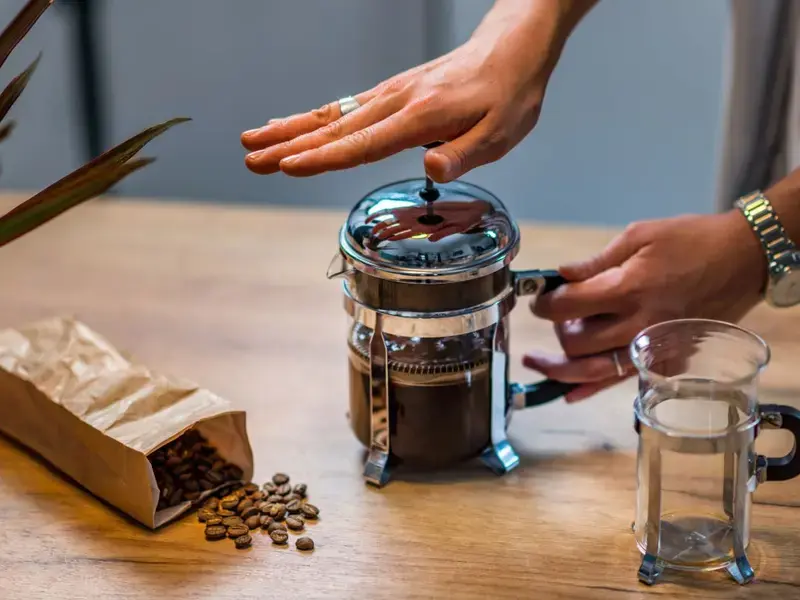 A woman using a French press to brew coffee.