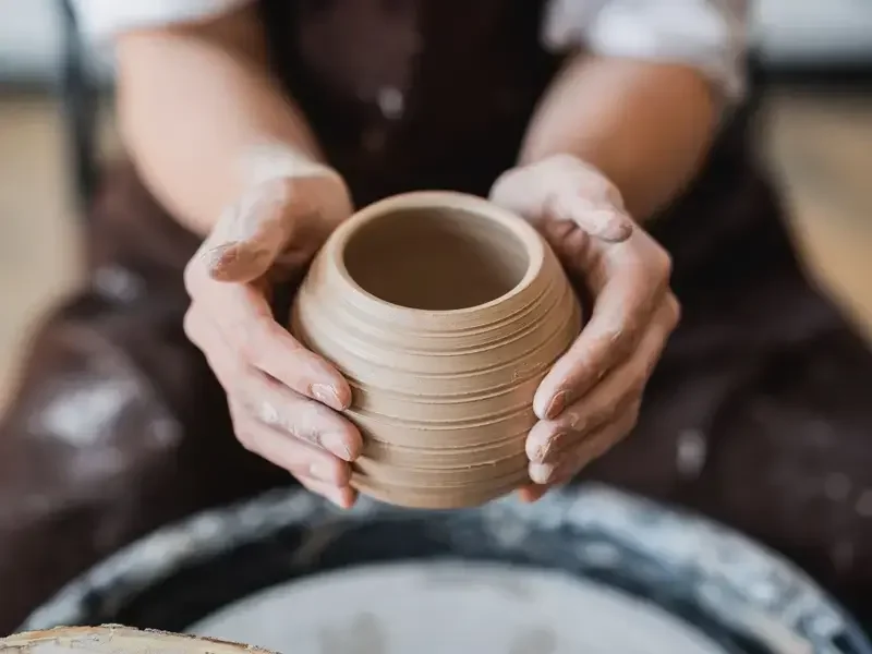 two hands lifring up a ceramic cup that's just made on a potter's wheel