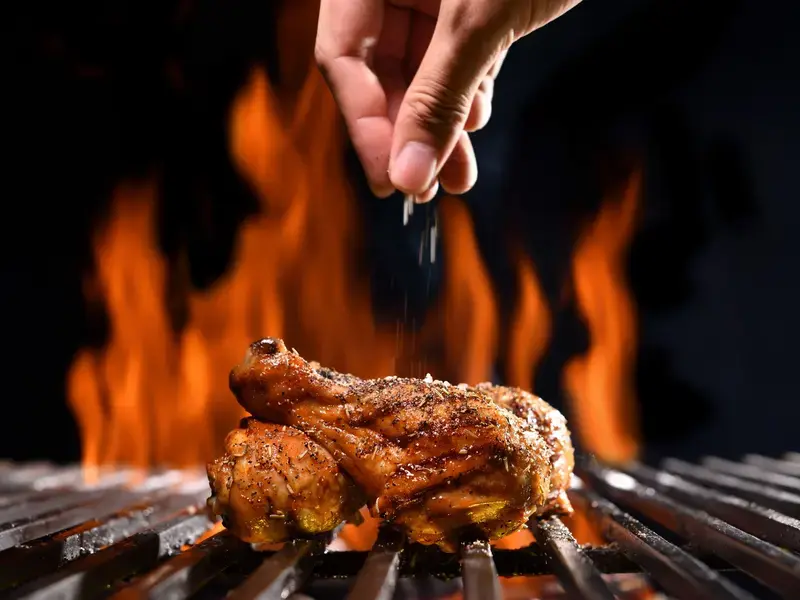 Chicken on the barbecue being seasoned.