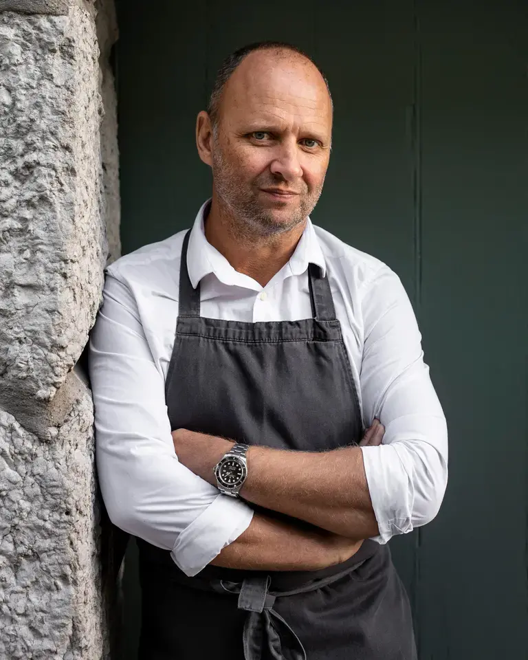 Chef Simon Rogan leaning against a stone wall.