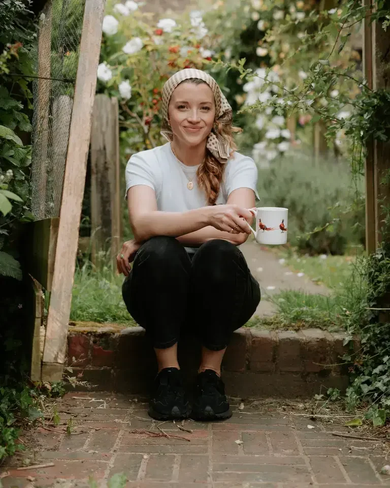 Lucy Sally Sommer sitting on a garden step, holding a mug.