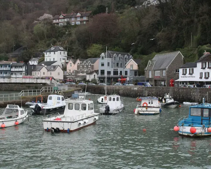 Small harbor with fishing boats, colorful houses, and lush hills in the background on a cloudy day.
