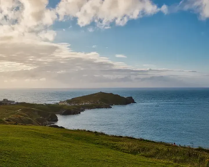 Grassy coastal headland extending into the sea under a partly cloudy sky with distant ocean views