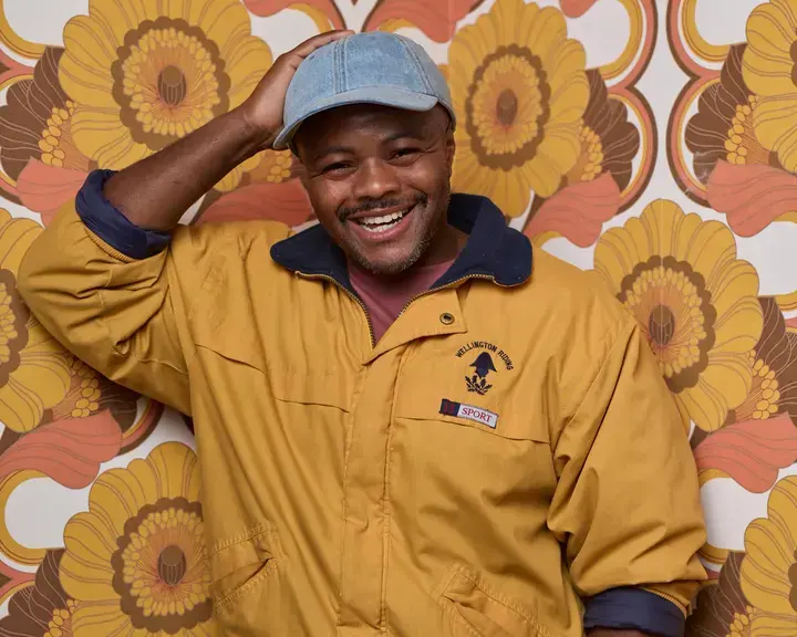 Chef Dom Taylor smiling against colourful wallpaper.
