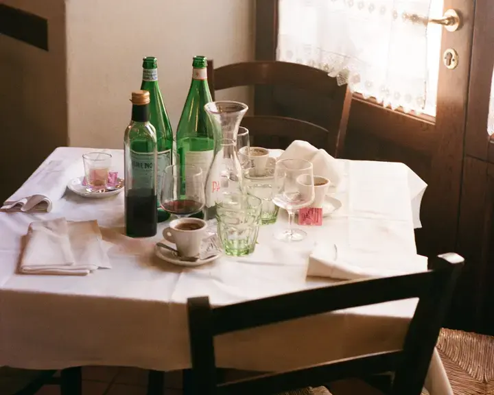 A restaurant table with empty water bottles, wine glasses and coffee cups.